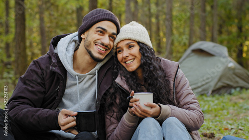 Happy married couple drinking hot drink outdoors in autumn forest young hikers resting in nature at campsite people in love communicate enjoy carefree relationship celebrate anniversary romantic date