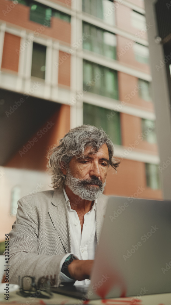 Clouse up, mature businessman with beard in eyeglasses wearing gray jacket sits on cafe. Middle aged manager successful man user on laptop pc computer sit at cafe outdoors Clouse up, mature businessman with beard in eyeglasses wearing gray jacket sits on cafe. Middle aged manager successful man user on laptop pc computer sit at cafe outdoors