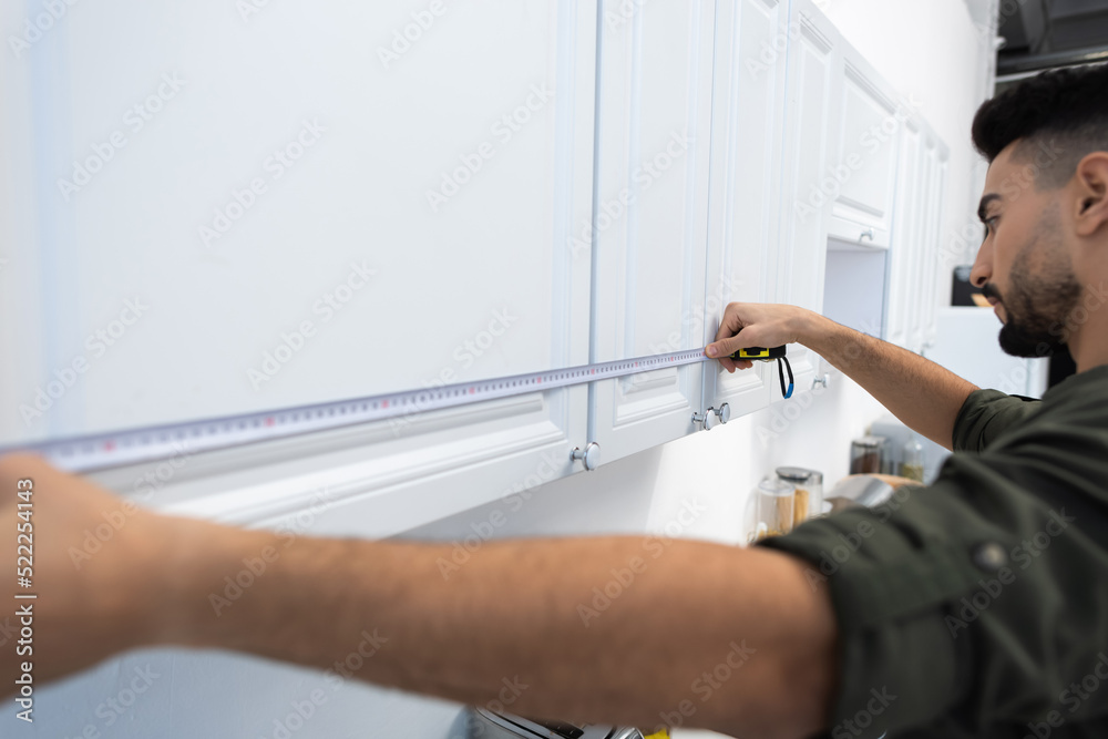 Side view of arabian man measuring cupboards in kitchen Side view of arabian man measuring cupboards in kitchen