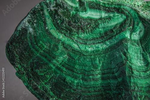 Malachite chunk stone on top of the silver surface. Randomly shaped green stone with waves and shades of green color. Malachite is a green copper carbonate mineral.Mixture of green colors