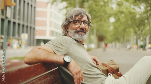 Foto Positive middle-aged man with gray hair and beard wearing casual clothes sits on bench