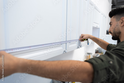 Side view of arabian man measuring cupboards in kitchen