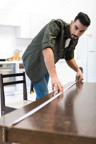 Arabian carpenter measuring blurred wooden table in kitchen