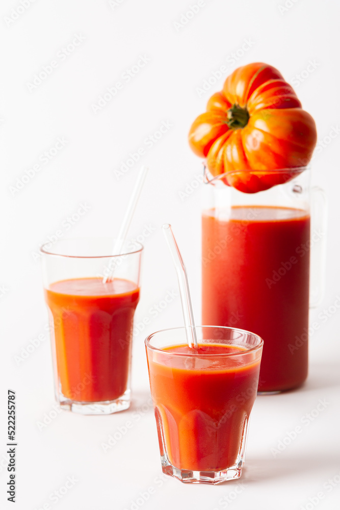 Homemade freshly squeezed tomato juice in glasses and a jug with tomatoes on a white background Homemade freshly squeezed tomato juice in glasses and a jug with tomatoes on a white background