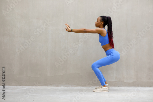 Image of sporty athletic woman in sneakers and tracksuit squatting doing sit-ups in gym isolated over gray background © Home-stock