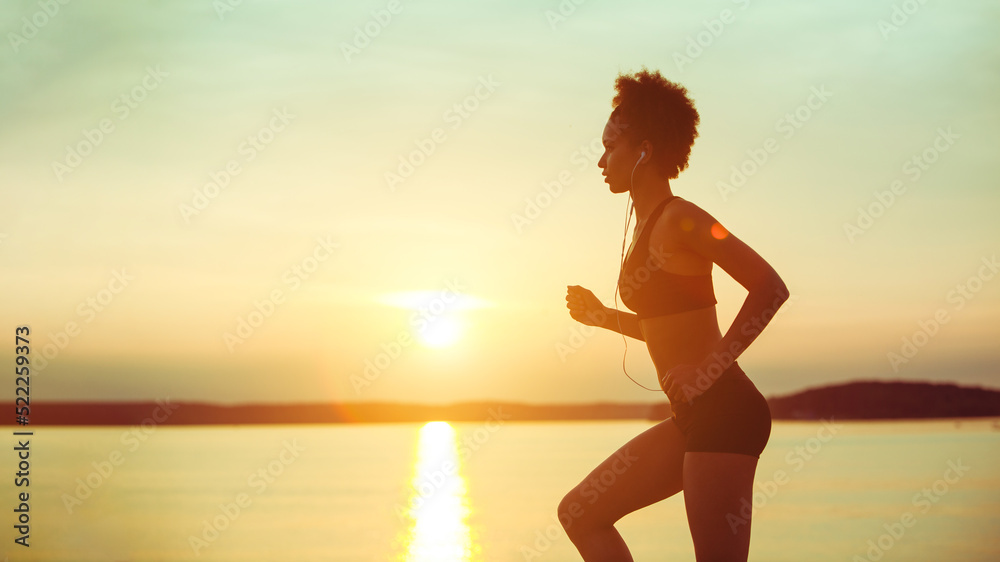 Attractive young African girl athlete running at sunset along the beach. Fitness training of runner