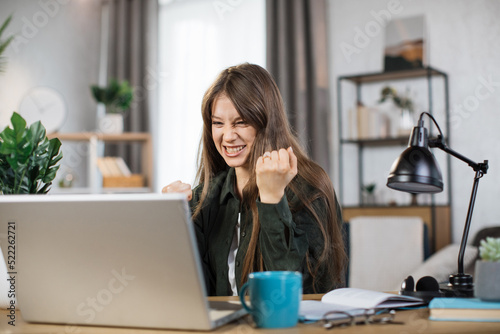 Free Download Happy caucasian woman student in casual wear sitting at table with modern laptop and keeping arms raised. Concept of people, technology and distance learning and success. - GFXLoad