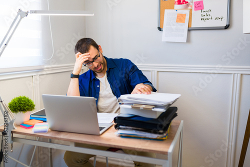 Tired man feeling overwhelmed while sitting at his work desk at home