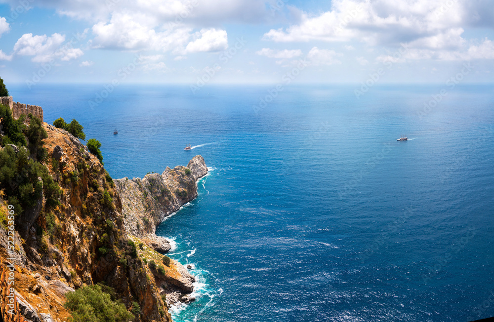 Beautiful image from a high cliff to endless expanse of blue sea sparkling in sun against light blue sky. Picturesque rock in mediterranean sea.