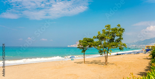 Beautiful beach of Mediterranean resort town Alanya Turkey with blue skies, expanse of sea and tree on sand beach. Natural seascape on bright sunny day.