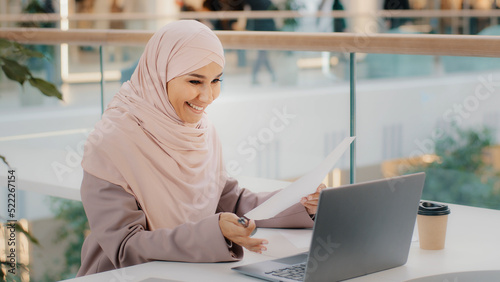 Fotografiet Young islamic woman sitting in cafe conducting online lesson talking on video co