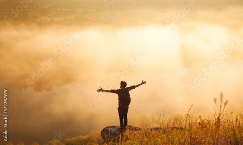 male hiker standing on mountain slope with outstretched arms at sunrise © kegfire