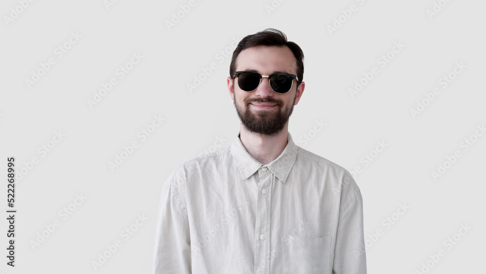 Close-up portrait of a handsome smiling young man with beard in sun glasses. Joyful student or freelancer isolated on gray background studio shot Close-up portrait of a handsome smiling young man with beard in sun glasses. Joyful student or freelancer isolated on gray background studio shot