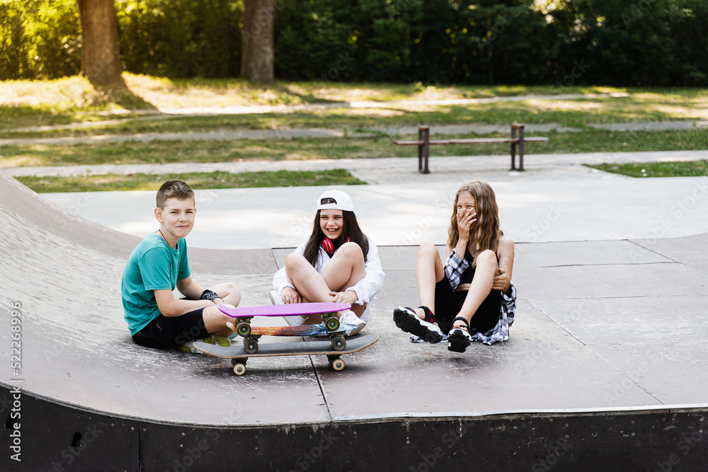 Children with skateboard and penny boards communicate and discuss on the sports playground. Children friendship concept. Children smile and laugh and have fun together. Children with skateboard and penny boards communicate and discuss on the sports playground. Children friendship concept. Children smile and laugh and have fun together.