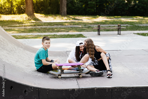 Children with skateboard and penny boards communicate and discuss on the sports playground. Children friendship concept. Children smile and laugh and have fun together.