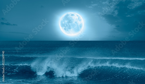 Night sky with blue moon in the clouds sea wave in the foreground  Elements of this image furnished by NASA