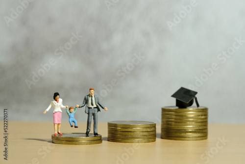 Miniature people toy figure photography. Couple with baby child walking above coin money stair to the cap. Future financial plan for education concept