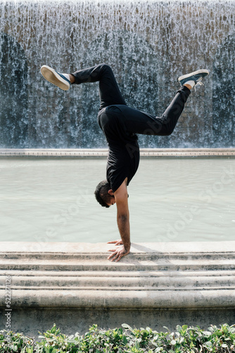 Fototapeta Naklejka Na Ścianę i Meble -  Young latin guy doing the vertical in front of a fountain in Barcelona on a sunny day. Showing strength and determination.
