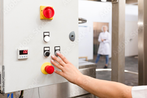 Buttons for controlling a mechanized line in an industrial bakery. Operators hand turns on process of kneading dough. View of operation panel and product inspection monitoring display