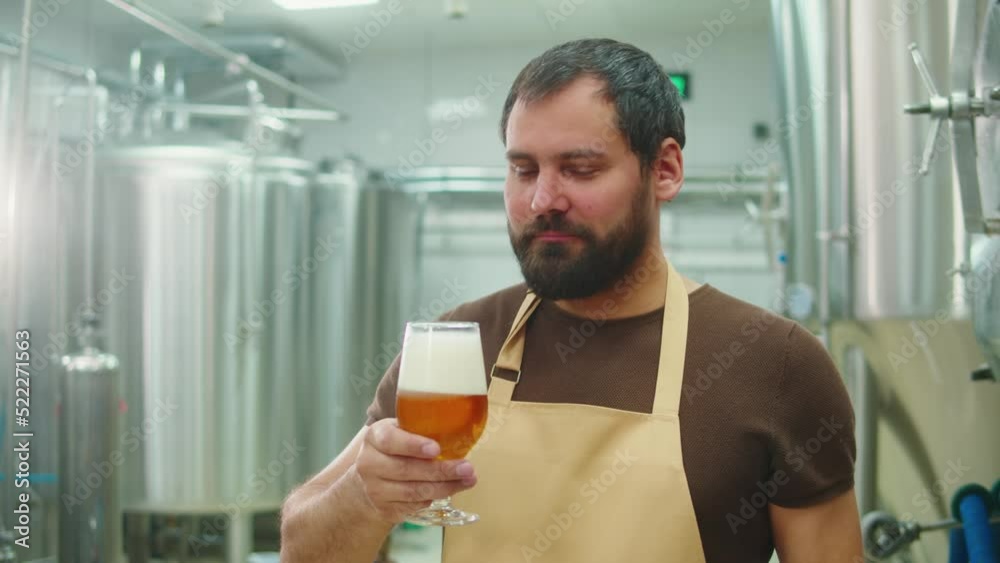 Craft beer production factory, brewery manufacture. Man trying beer in glass close-up. Brewer portrait, cooking alcohol in metal vats bottles. Craft beer production factory, brewery manufacture. Man trying beer in glass close-up. Brewer portrait, cooking alcohol in metal vats bottles.