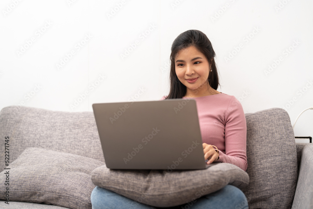 cheerful asian woman using laptop while sitting on sofa in living room cheerful asian woman using laptop while sitting on sofa in living room