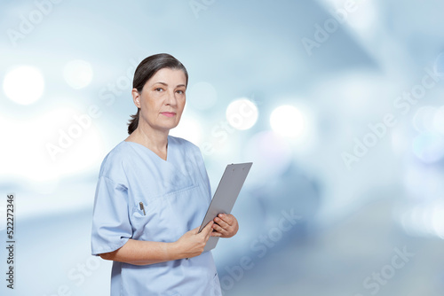 Portrait of a stern looking middle aged nurse in a blue scrub holding a clipboard, hospital interior background, blue filter effect. photo