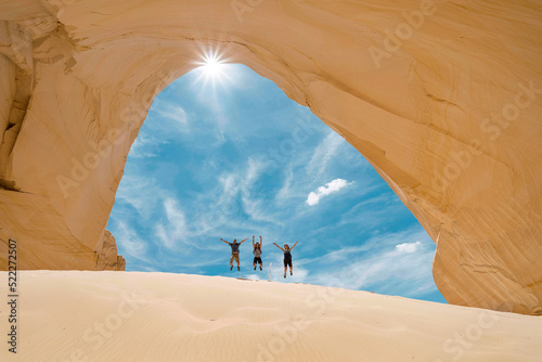Family jumping with joy in front of the entrance of a sand cave  photo