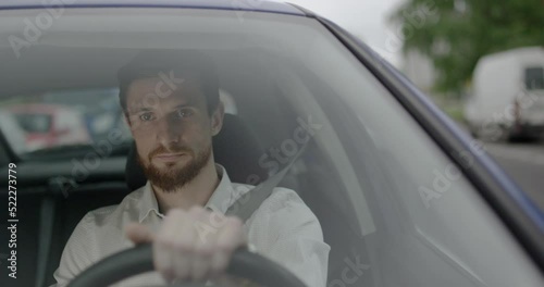 Young taxi driver with a beard is driving a car through the City during the day.