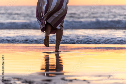Rear View of Woman Legs Walking on a Beach to the Ocean at Sunset Time.Copy Space