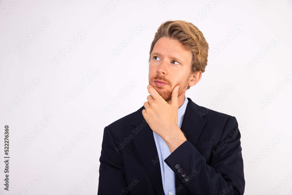 Portrait of pensive young businessman with hand on chin. Caucasian manager wearing blue shirt and black suit coat standing and thinking about something. Business issues concept Portrait of pensive young businessman with hand on chin. Caucasian manager wearing blue shirt and black suit coat standing and thinking about something. Business issues concept