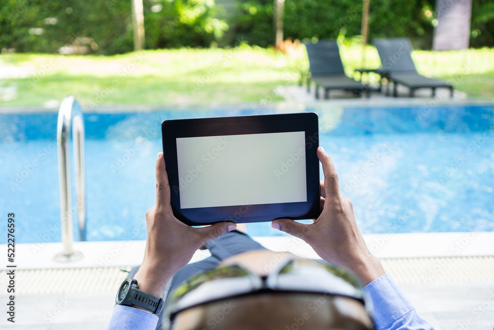 Business man holds tablet with isolated screen in his hands, blank white screen at swimming pool.