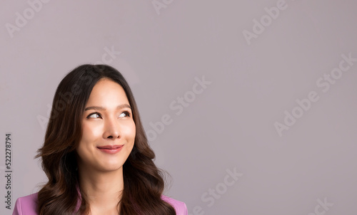 Asian woman long hair, wearing a pink suit is smiling and looking at the gray empty background.