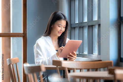 Asian young  woman working, using tablet in the cafe. Asian beautiful woman happy face smiling and have a good idea, sitting and using tablet in the cafe. © Darunrat