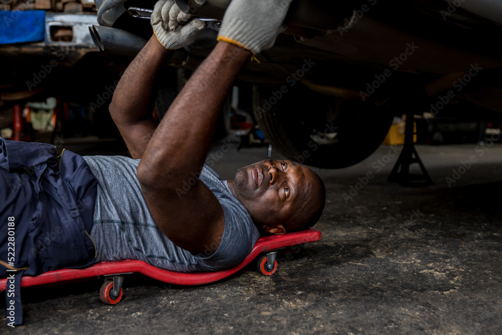 Mechanic lying down and working under car at auto service garage. Technician vehicle maintenance and checking under car at automotive motor garage.
