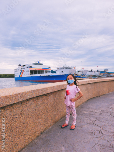 Ferry at the jetty with little girl wearing face mask nearby.