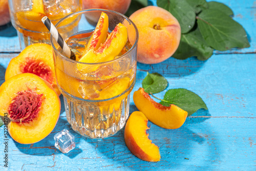 Homemade peach ice tea with ripe fresh peaches on high-colored blue wooden background