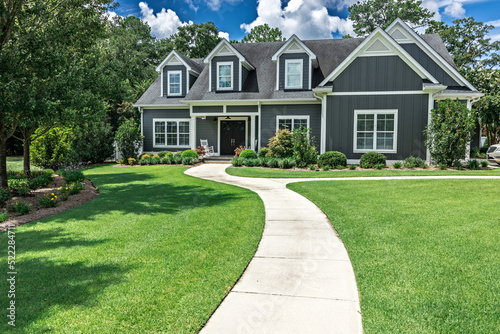 A large gray craftsman new construction house with a landscaped yard and a long leading walkway to the front door