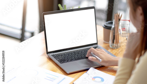 Mockup image of a woman using and typing on laptop computer with blank white desktop screen on wooden table