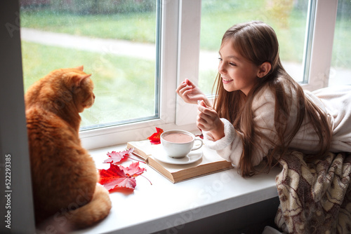 Foto Little girl in warm terry robe lying on window sill and reading a book