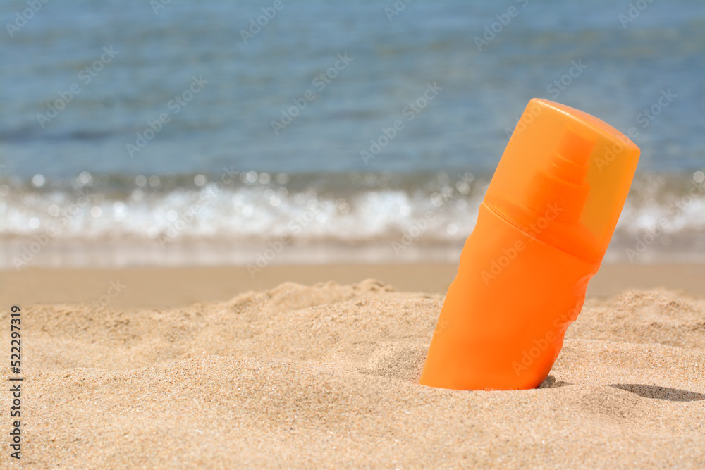 Bottle with sun protection spray on sandy beach near sea, space for text Bottle with sun protection spray on sandy beach near sea, space for text