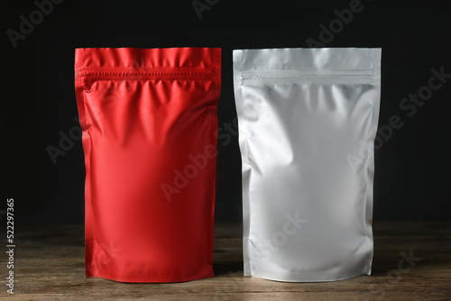 Different blank foil packages on wooden table against dark background