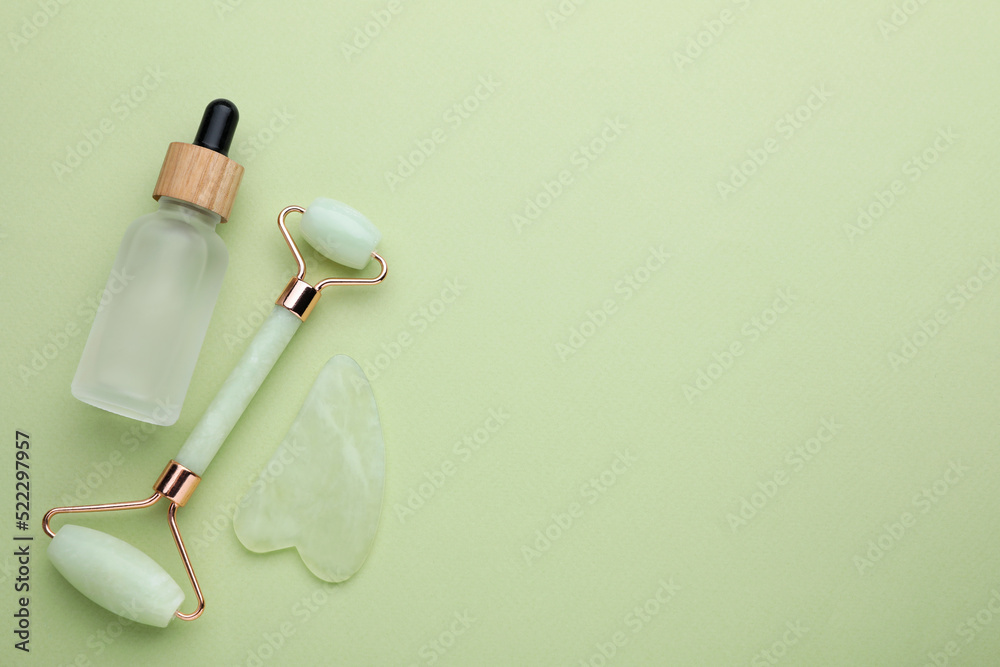Jade gua sha tool , facial roller and bottle of serum on light green background, flat lay. Space for text Jade gua sha tool , facial roller and bottle of serum on light green background, flat lay. Space for text