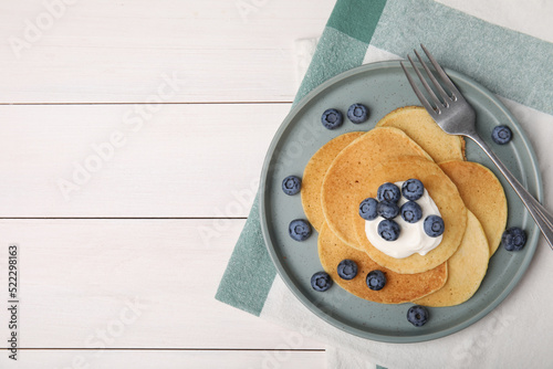 Tasty pancakes with natural yogurt and blueberries on white wooden table, flat lay. Space for text