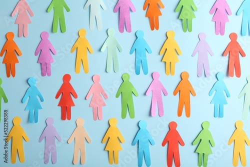 Many different paper human figures on light blue background, flat lay. Diversity and inclusion concept