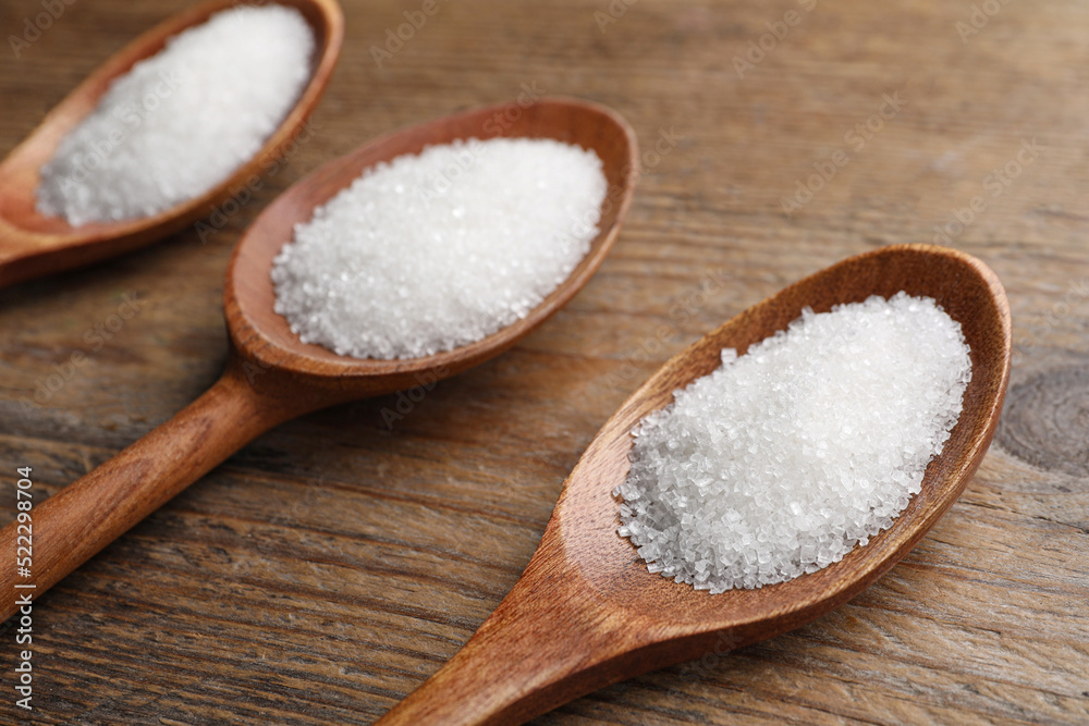 Granulated sugar in spoons on wooden table, closeup Granulated sugar in spoons on wooden table, closeup