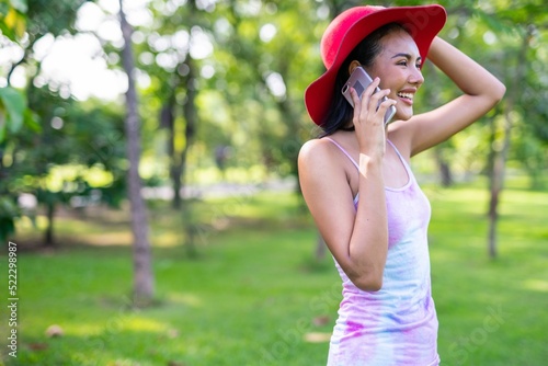 Portrait photo of the beautiful moment of a young asian beautiful lady with red hat happily chatting on her phone with her friends during a garden park strolling