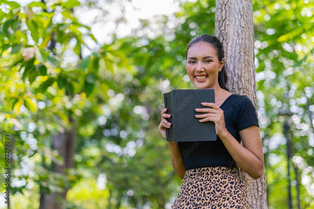 Portrait photo of the moment of a young beautiful asian female lady reading a book under a tree in an outdoor park during her summer holidays Portrait photo of the moment of a young beautiful asian female lady reading a book under a tree in an outdoor park during her summer holidays