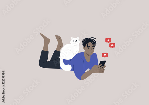 A young male African character lying on their stomach and checking their mobile phone notifications, a cat sitting on their back