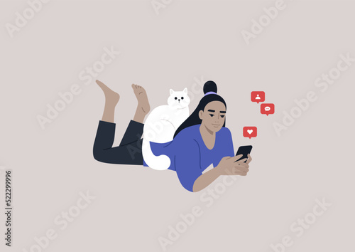 A young female Asian character lying on their stomach and checking their mobile phone notifications, a cat sitting on their back