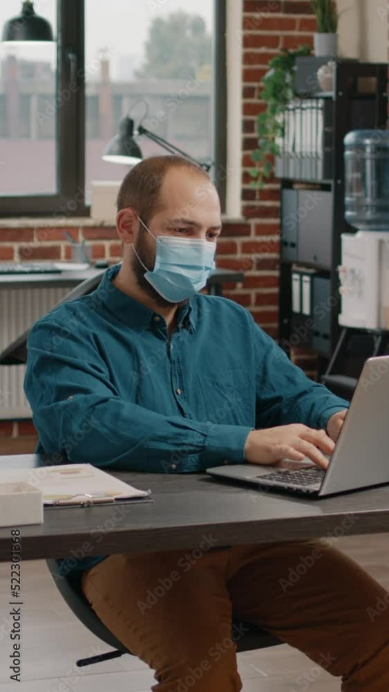 Employee checking data rate charts on papers and laptop, looking at display and wearing face mask. Business man using technology to plan project for presentation and startup meeting Employee checking data rate charts on papers and laptop, looking at display and wearing face mask. Business man using technology to plan project for presentation and startup meeting